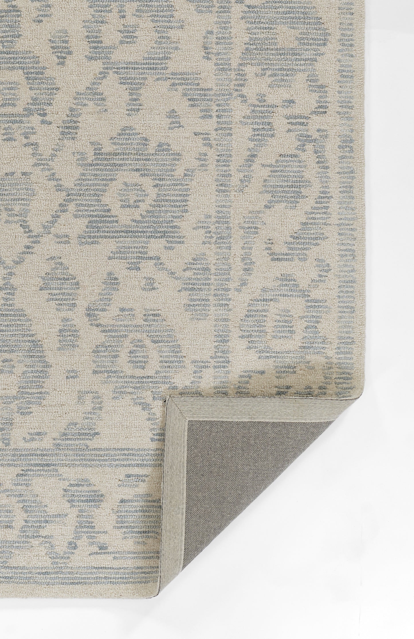 Beige rug with pale blue damask pattern; rectangular, folded corner reveals gray non-slip backing.