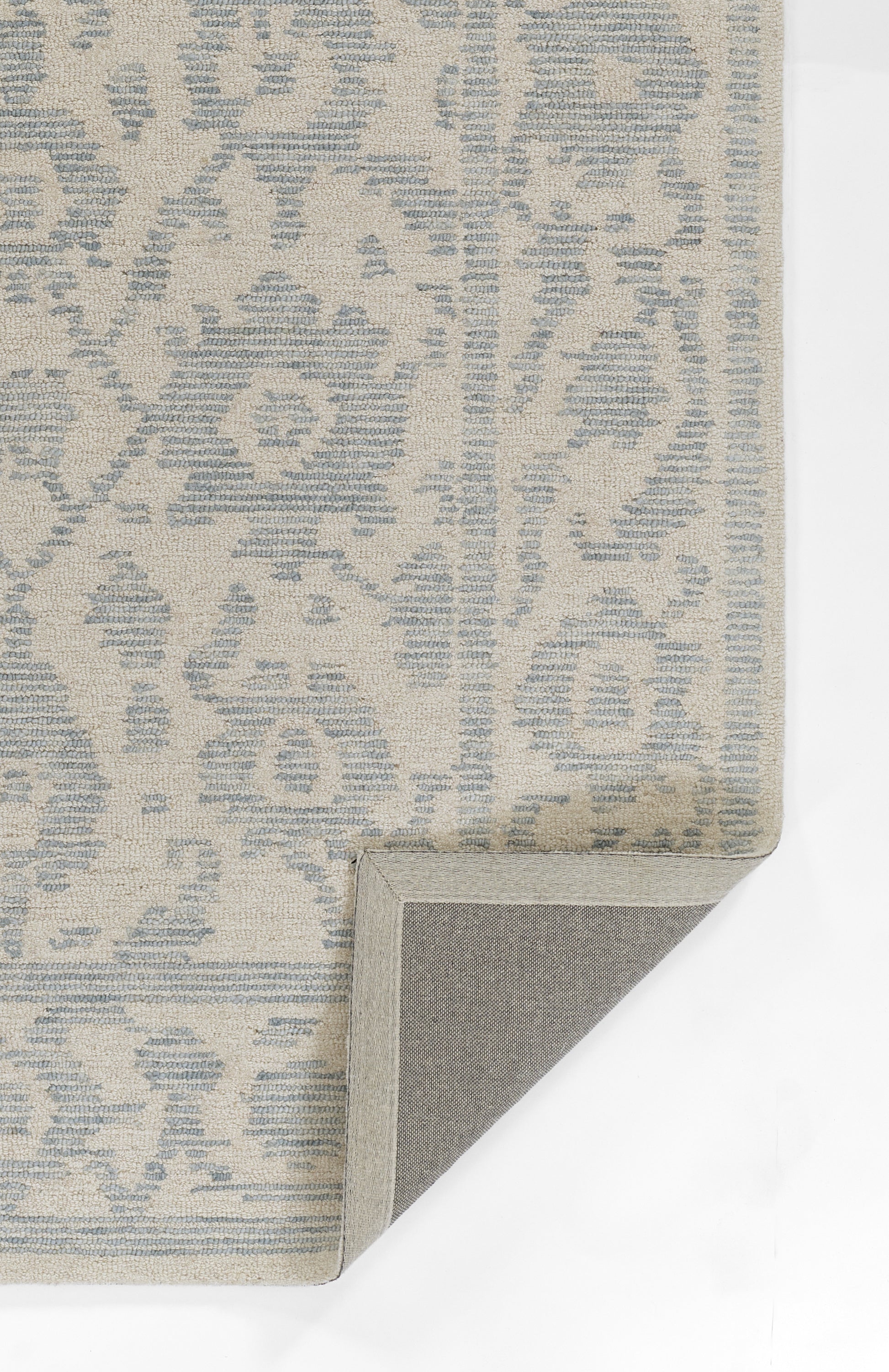 Beige rug with pale blue damask pattern; rectangular, folded corner reveals gray non-slip backing.