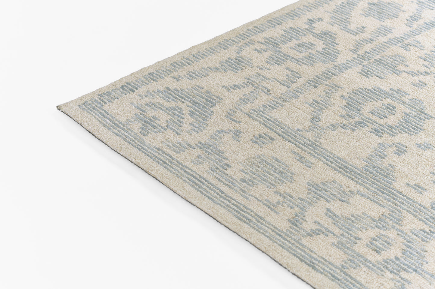 Beige rug with light blue damask pattern, rectangular decorative rug, corner view.