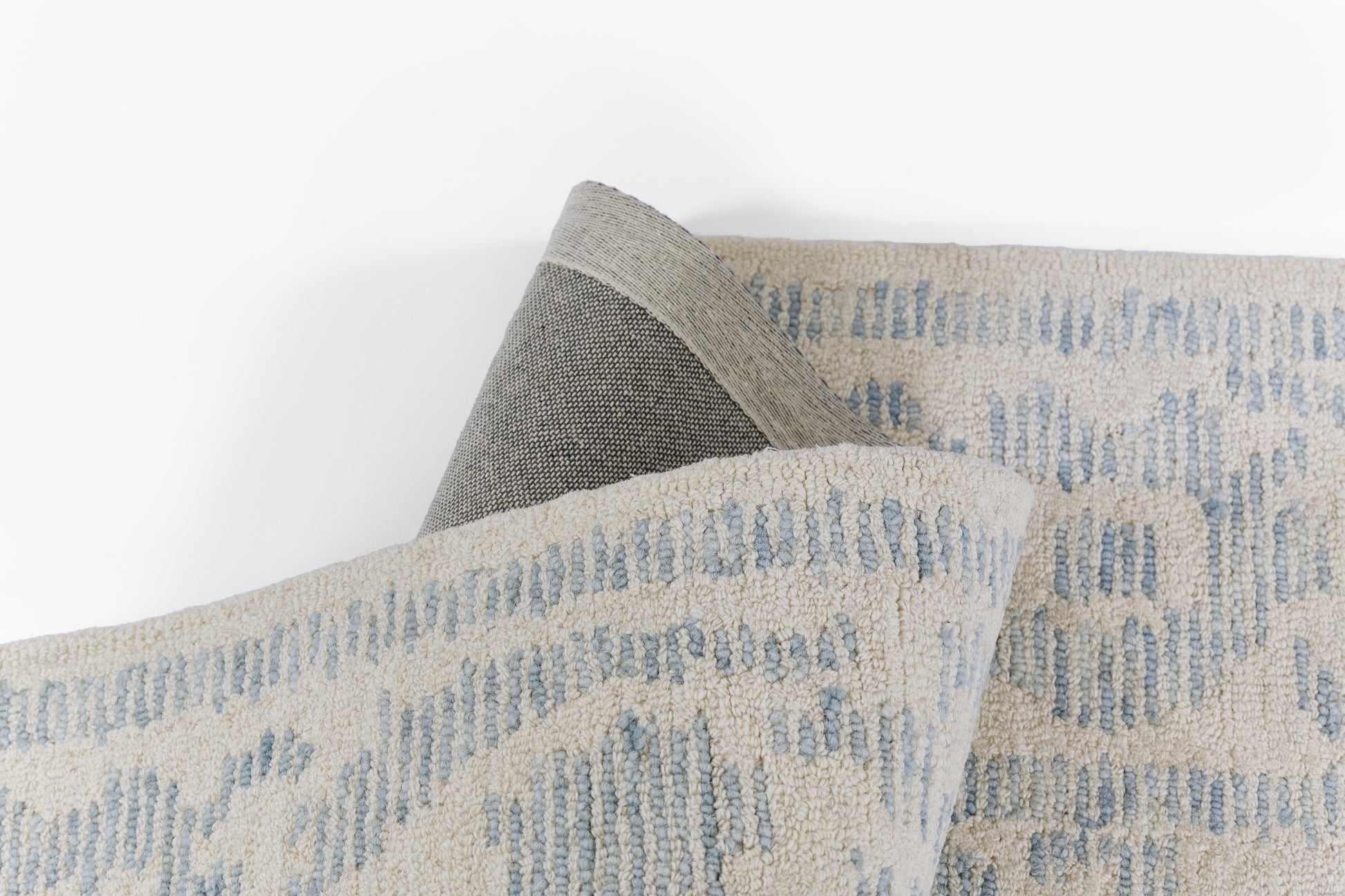 Beige woven rug with pale blue arc pattern and grey edge, folded to show texture, 2' x 3'.