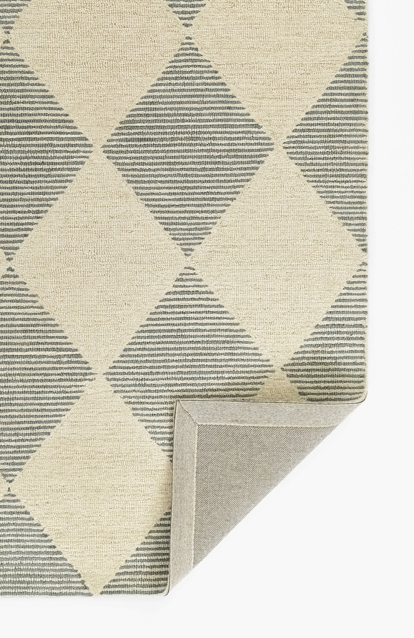 Geometric diamond-pattern rug in beige & blue-gray; woven textile with striped diamonds; folded corner shows gray backing.