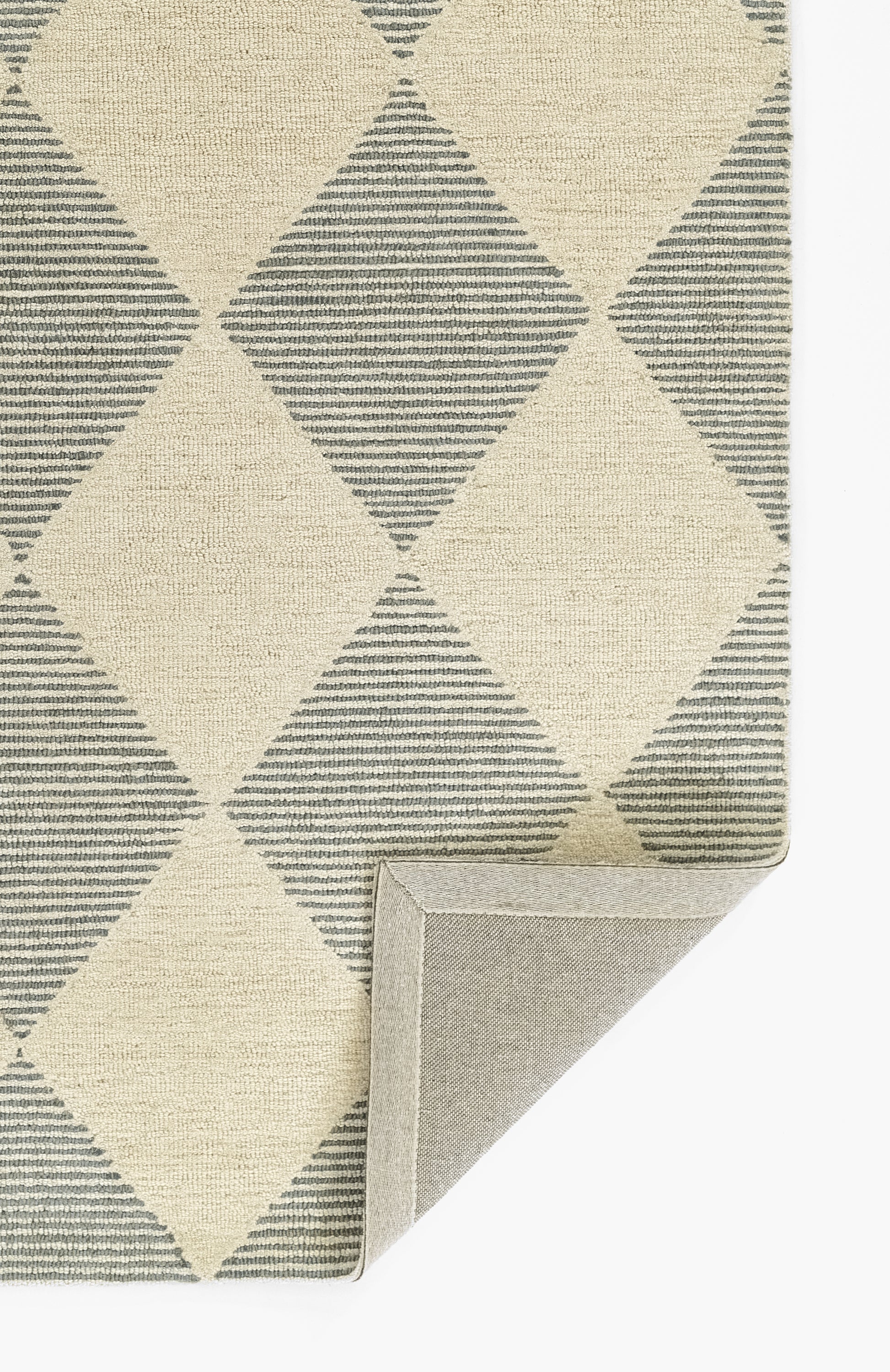 Geometric diamond-pattern rug in beige & blue-gray; woven textile with striped diamonds; folded corner shows gray backing.