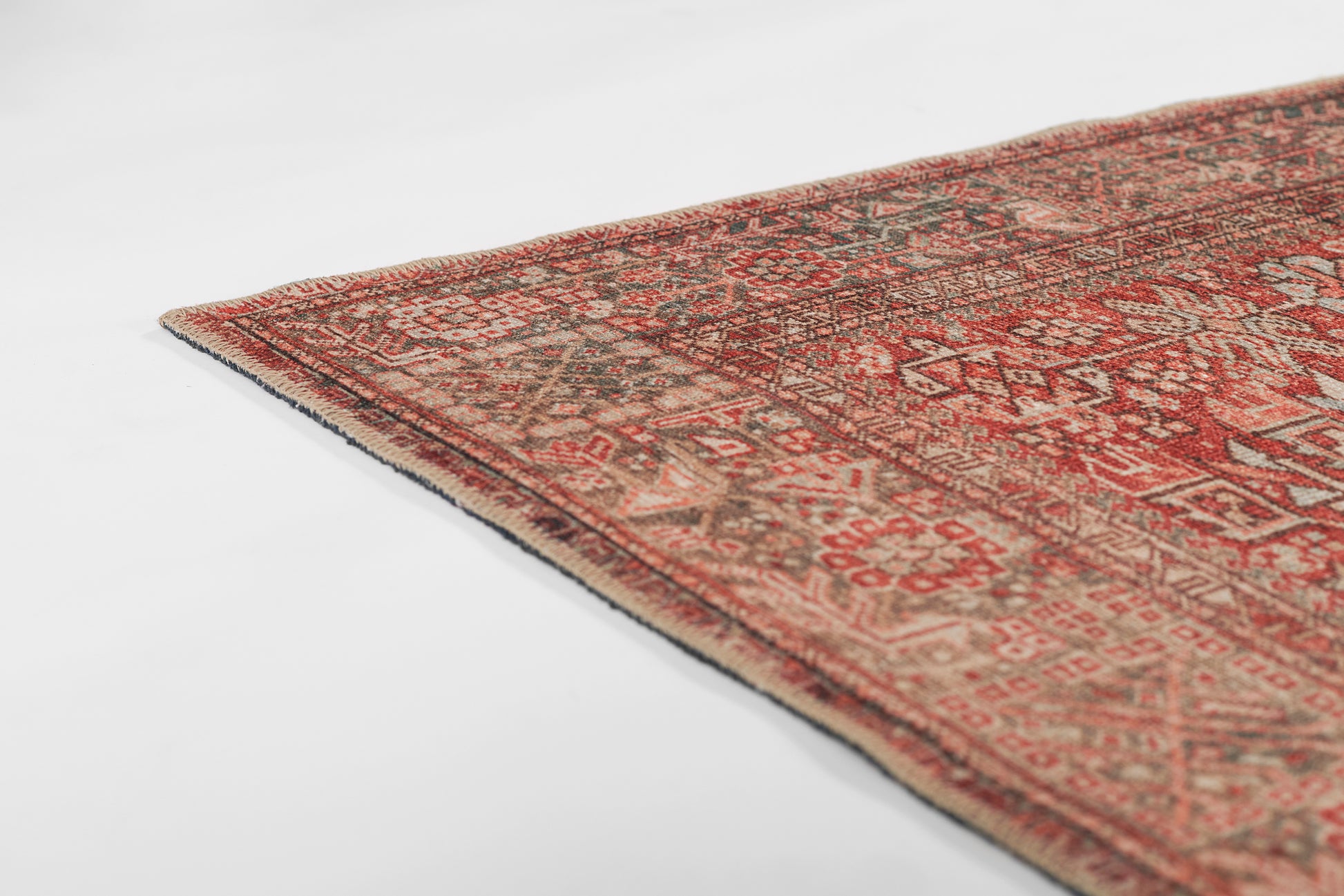 Red-toned oriental rug corner with beige geometric patterns and fringed edge.