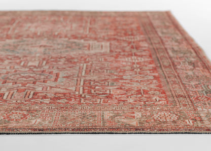 Red oriental wool rug with geometric ivory and green accents; distressed vintage look, edge visible.