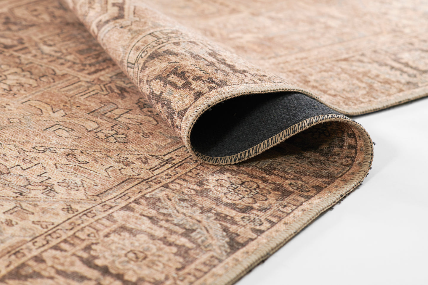 Beige & brown oriental rug with intricate geometric motifs; edge folded to reveal black underside.