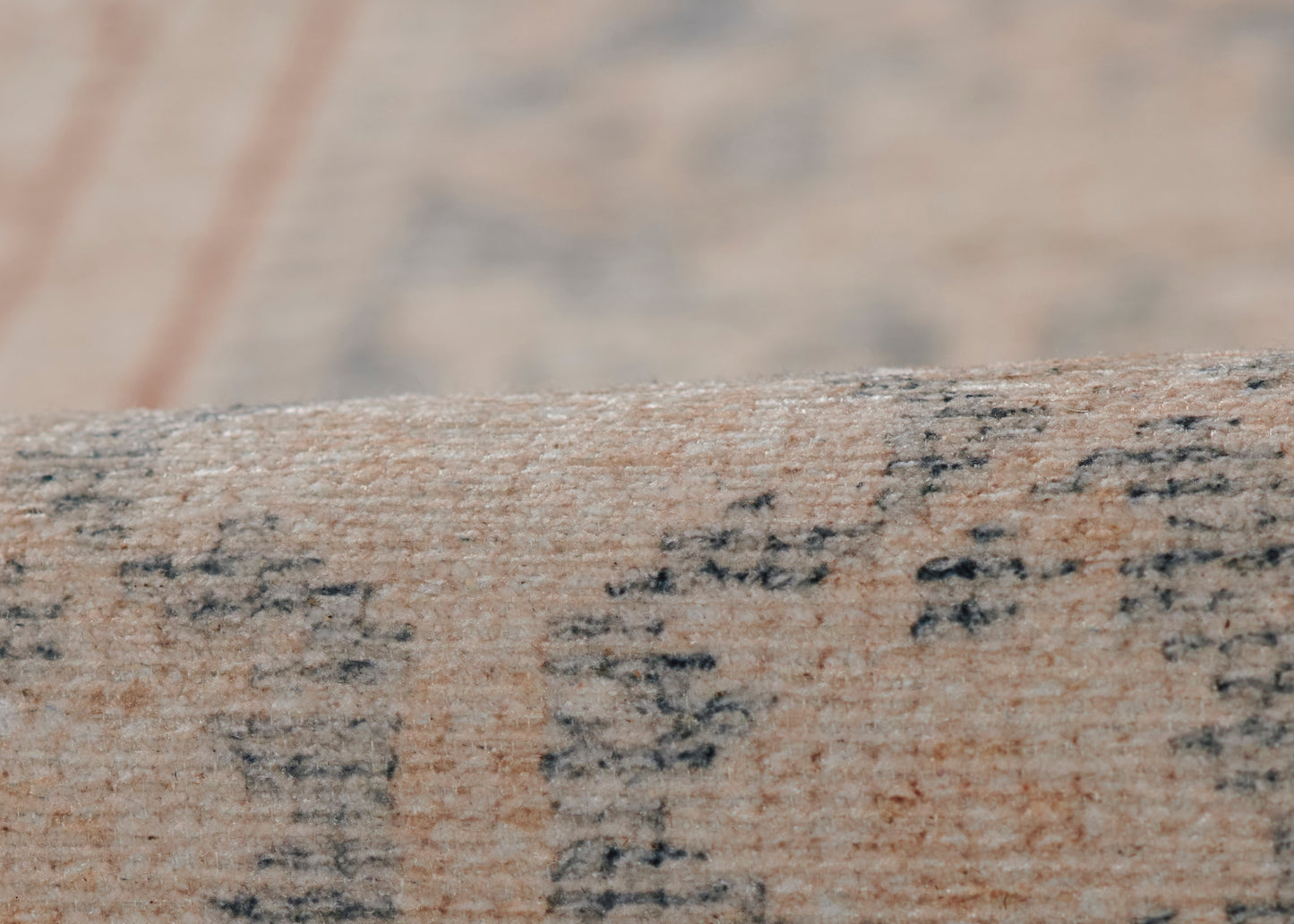 Beige woven runner rug with faded black script pattern and blue undertones; soft textile texture for floor decor.