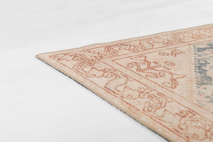 Corner view of a peach-beige patterned area rug with a geometric border and blue accents.