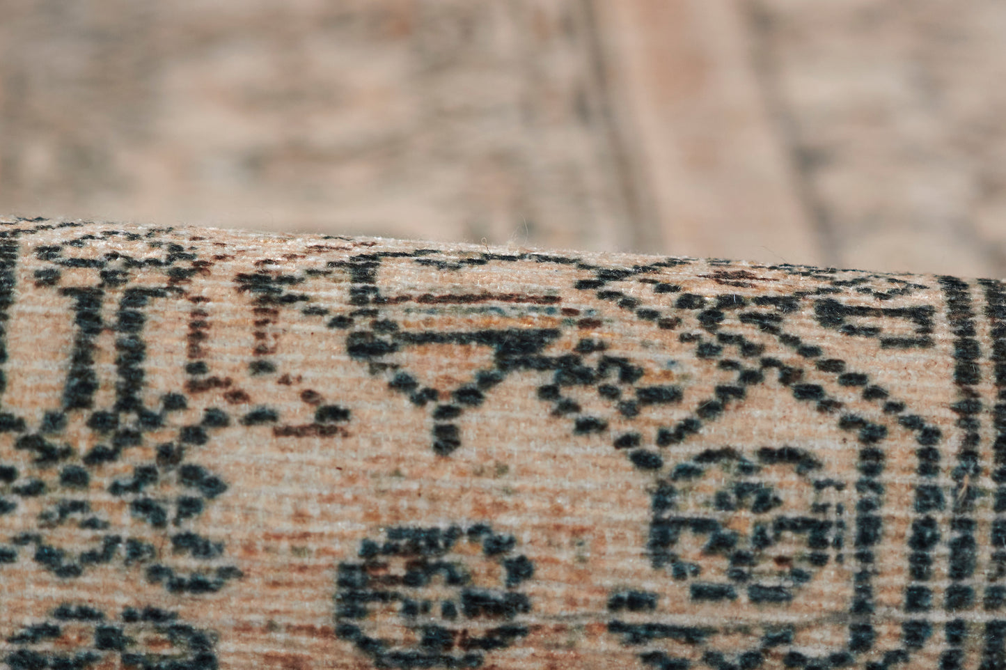 Close-up of beige rug with black geometric floral motifs and a visible woven border.