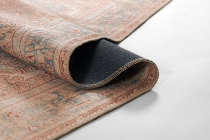 Persian-style woven rug in pink and beige with blue accents, rolled to reveal navy backing.