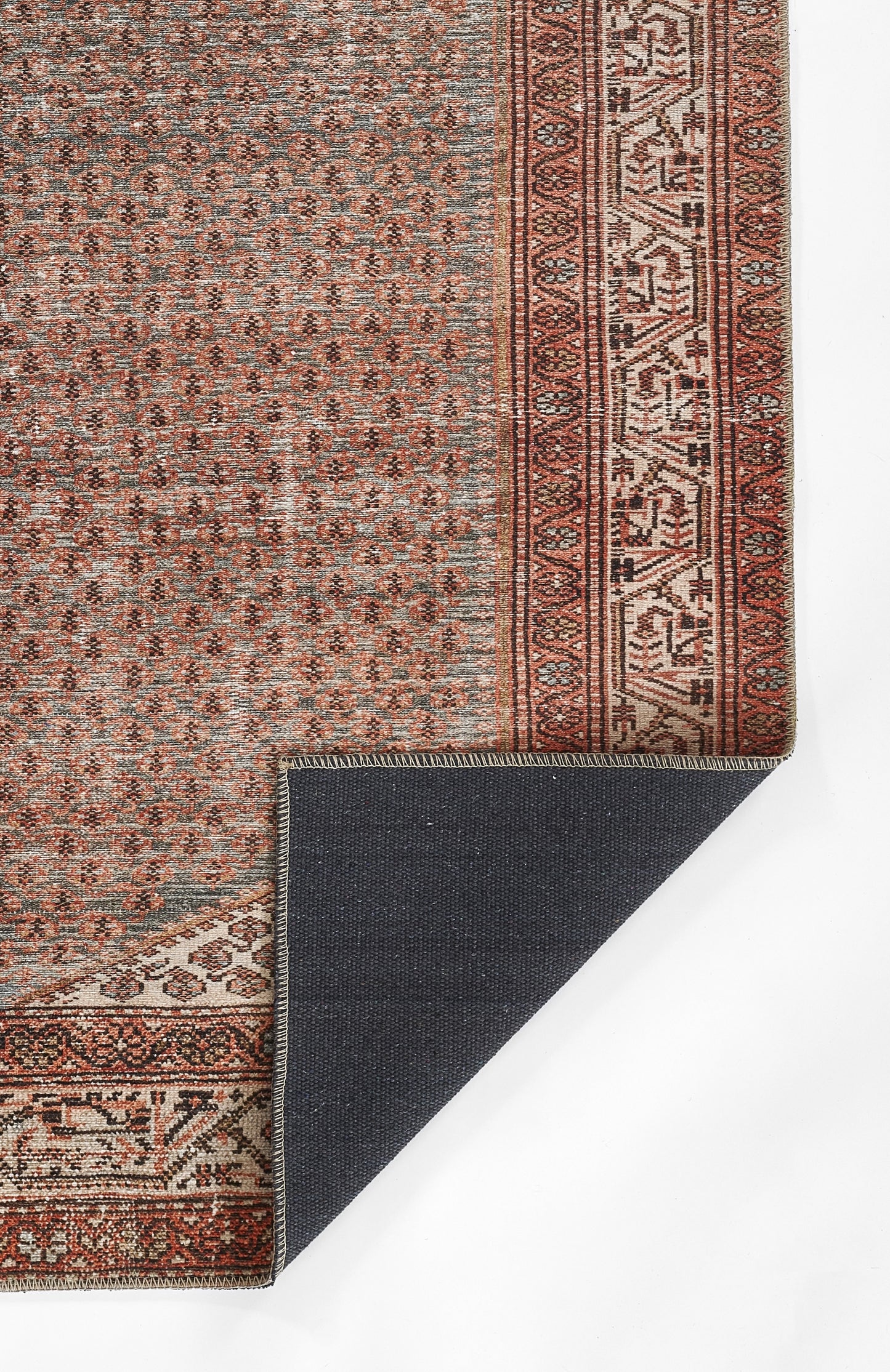 Persian-style rug with dusty blue field, red border and small repeating motifs; corner folded to reveal navy backing.