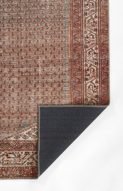 Persian-style rug with dusty blue field, red border and small repeating motifs; corner folded to reveal navy backing.