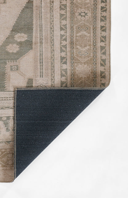Beige oriental-style rug with muted green and gray motifs; folded corner reveals dark blue denim-like backing.