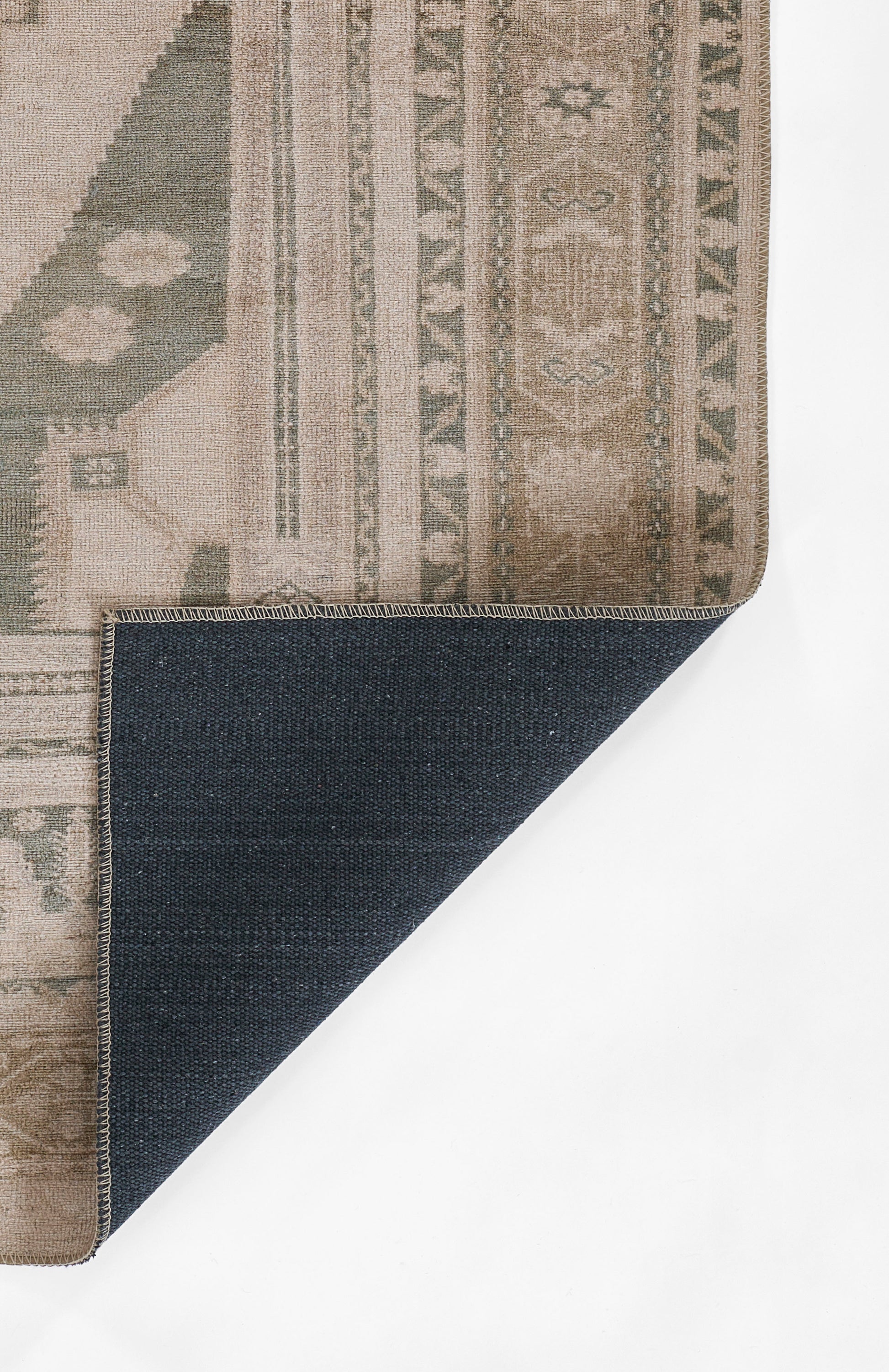Beige and sage geometric rug with decorative border; corner folded to reveal dark denim underside