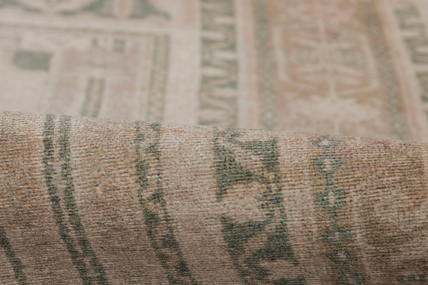 Rolled oriental-style rug in beige with green geometric motifs; woven wool texture.