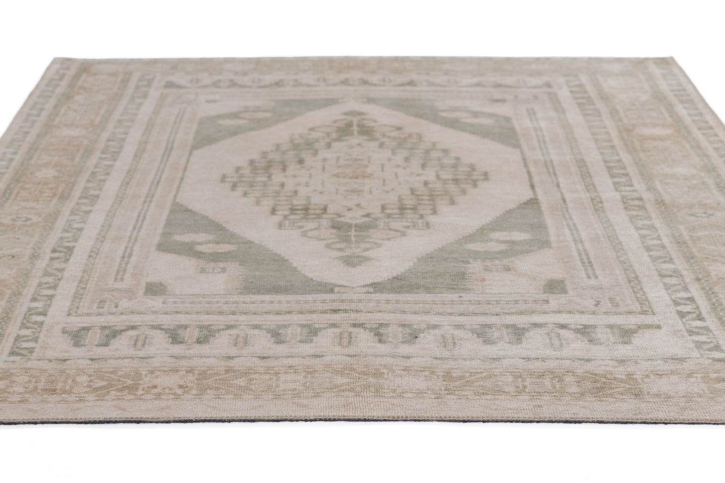 Light green-gray area rug with central diamond motif and subtle border, vintage-inspired geometric design.