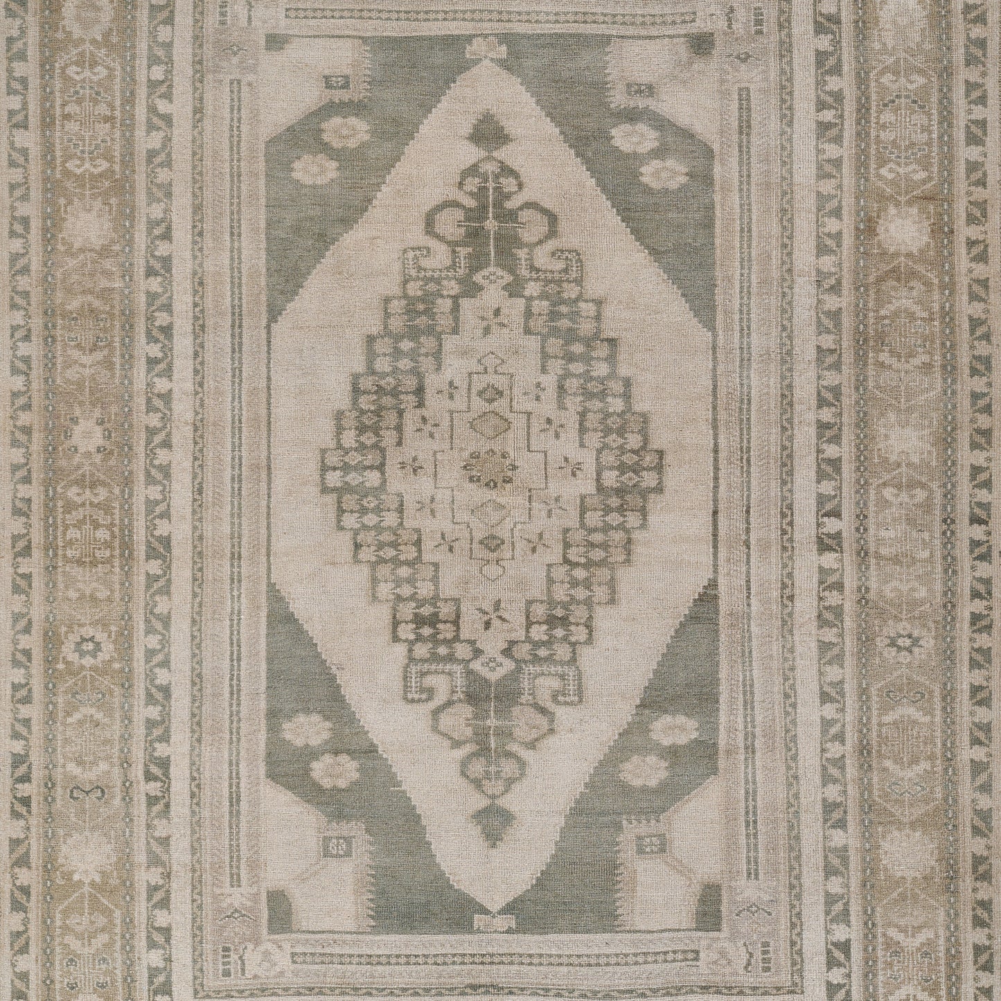 Rectangular woven rug in muted green and cream with central geometric medallion and decorative border, kilim-inspired.