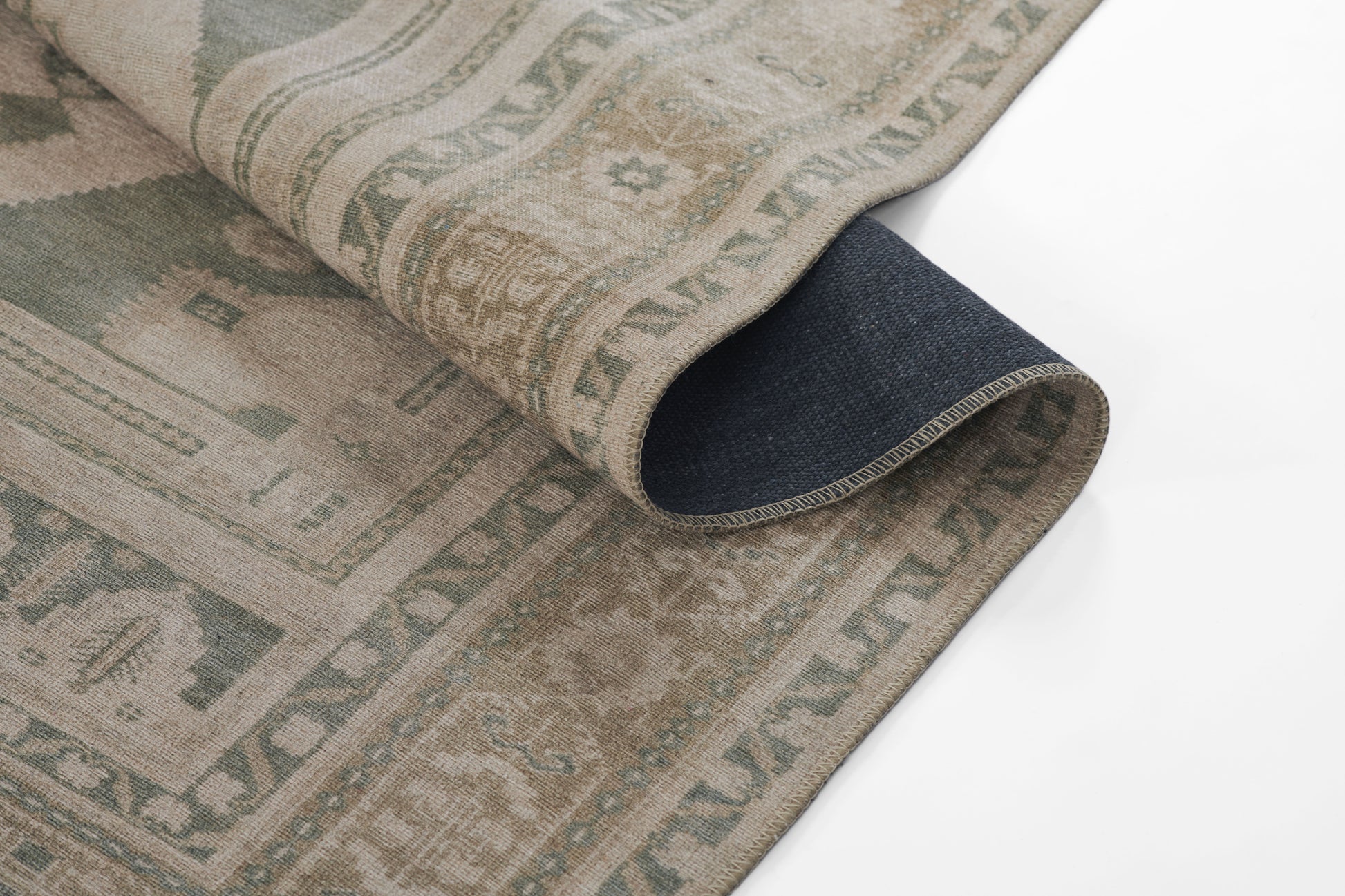 Green-beige geometric woven rug partially rolled, showing dark navy underside; modern kilim style for living room decor.