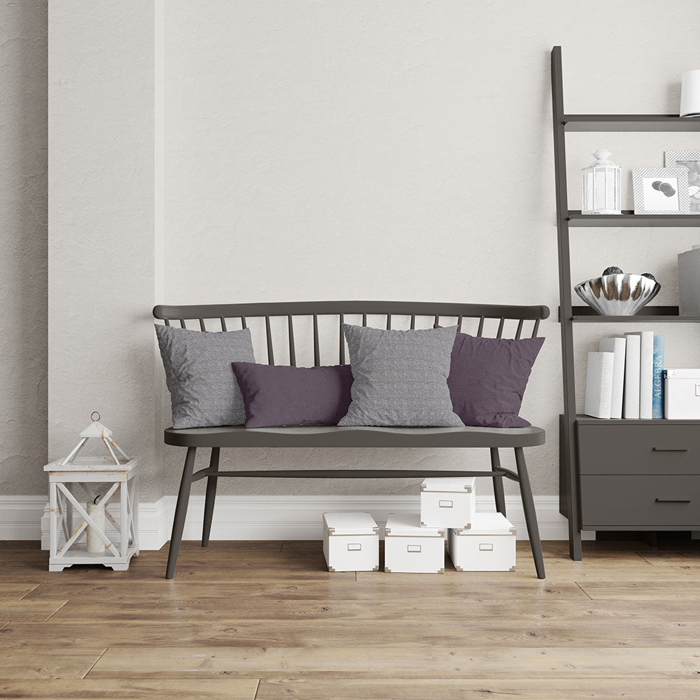 Dark gray metal bench with slatted back and gray and purple cushions, beside a lantern and a tall dark bookcase with decor.