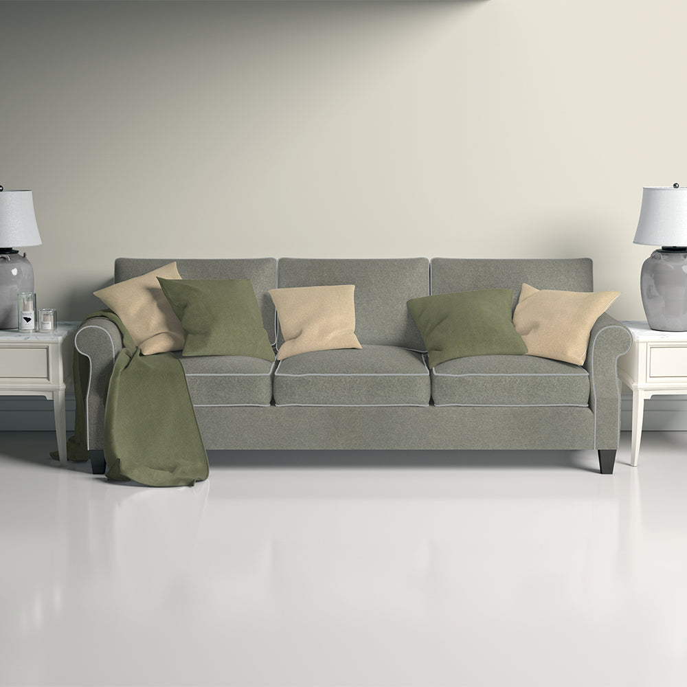 Grey upholstered sofa with beige and green cushions, green throw, flanked by side tables and lamps in a bright living room.