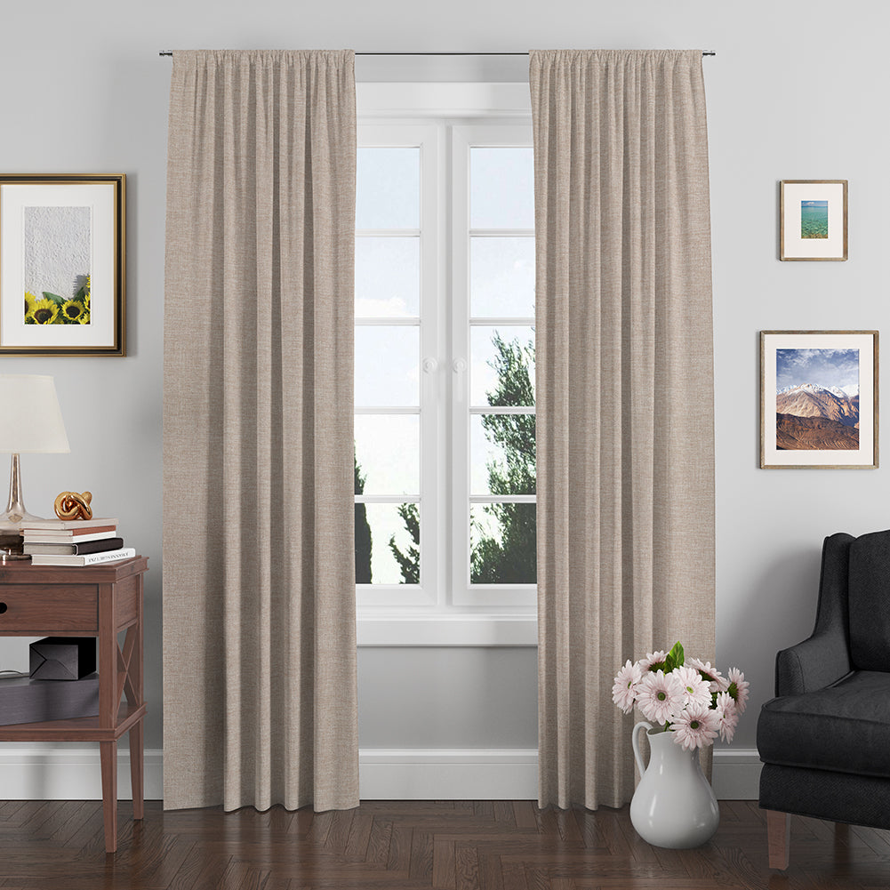 Beige textured floor-length curtain fabric framing a window in a cozy living room with wooden floor, lamp, art, and a vase.