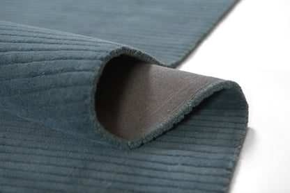 Teal blue ribbed rug with curled edge, corduroy-like texture and brown underside.