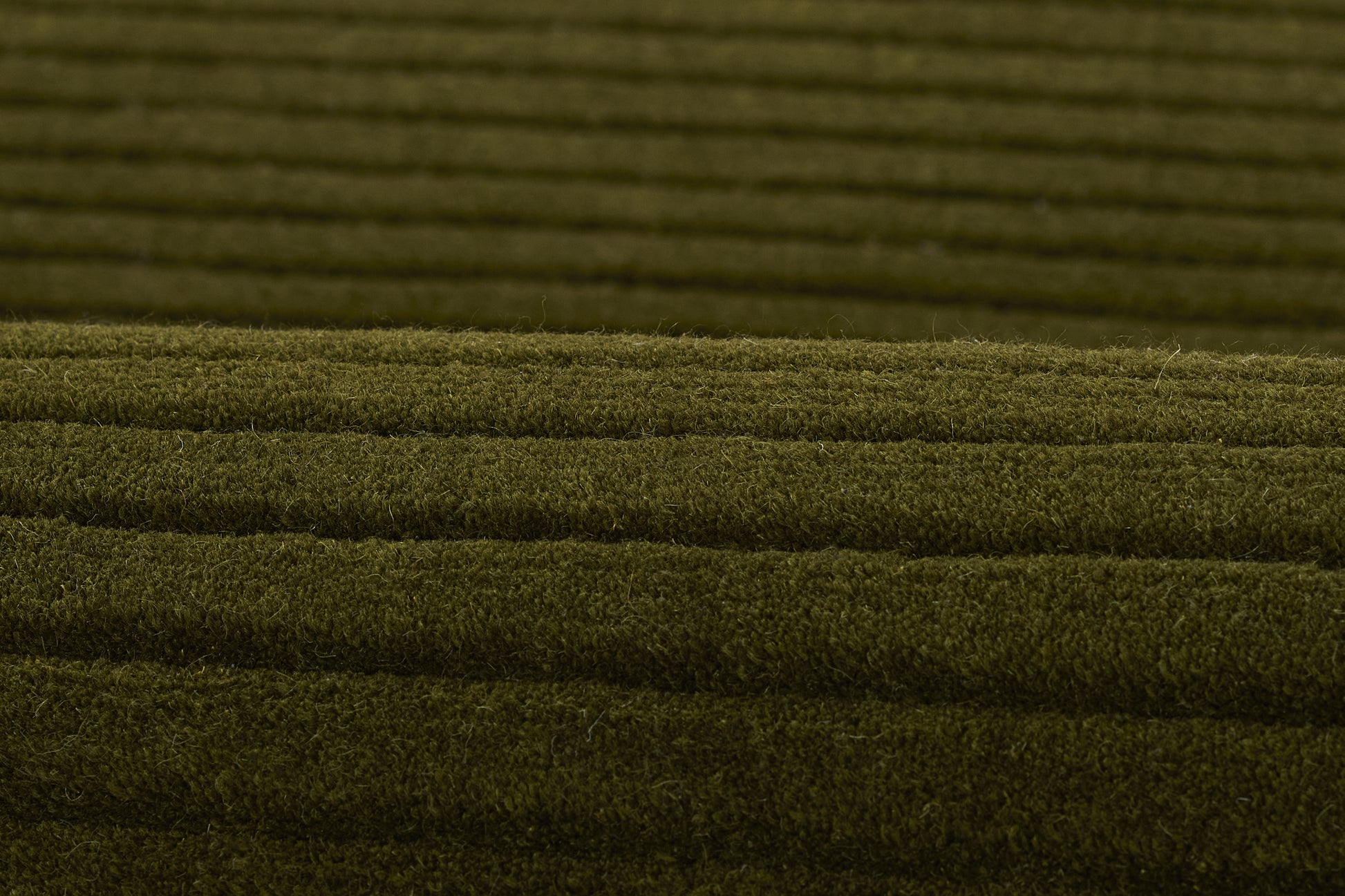 Olive-green ribbed carpet close-up, plush pile with horizontal ridges for flooring.
