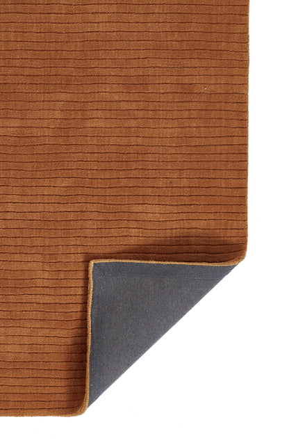 Rust brown ribbed rug with corduroy texture; folded corner reveals gray backing and tan edge.
