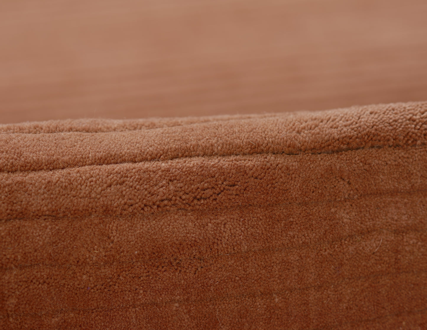 Close-up of caramel brown suede fabric with a stitched edge, plush texture on a wooden surface.