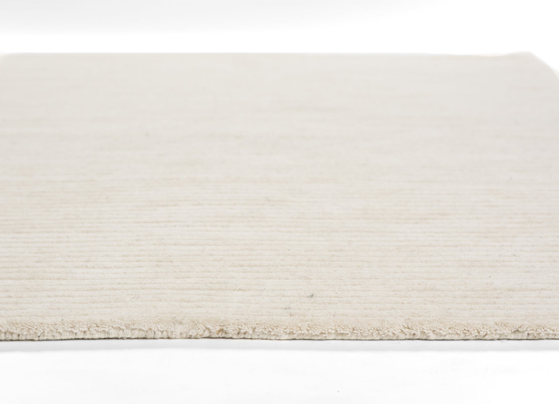 Cream-beige flat-weave rug with soft texture and short fringe along the edge.
