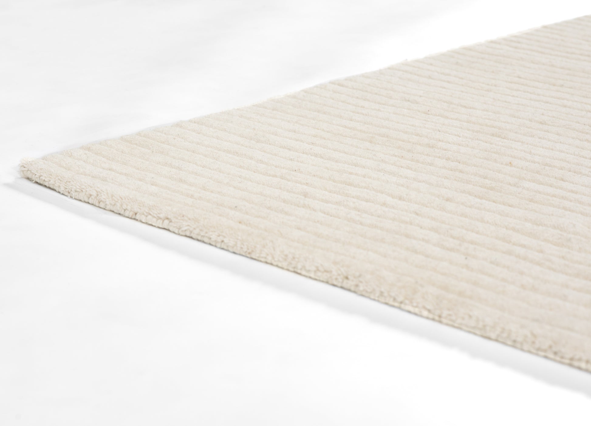 Cream ribbed rug with soft plush pile, visible edge, warm neutral beige.