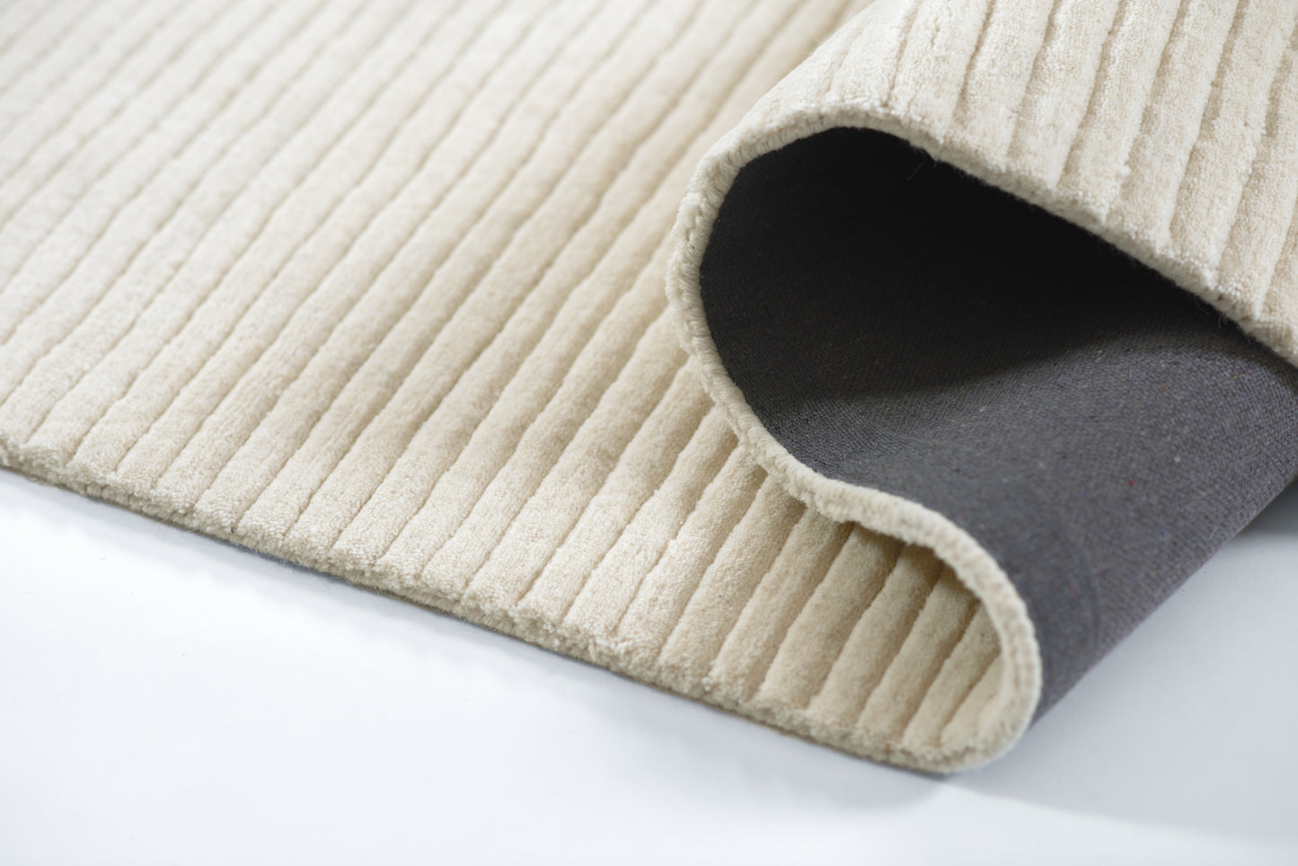 2' x 4' beige ribbed rug with dark backing, plush texture, rolled corner showing underside