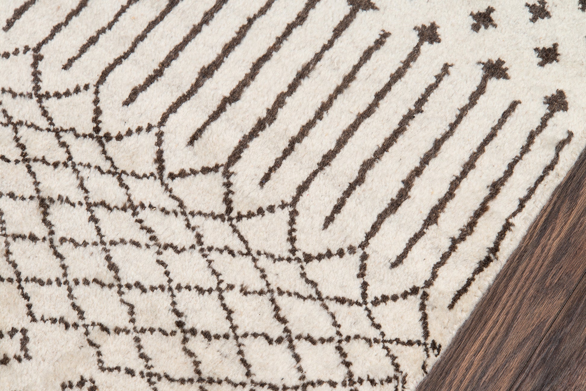 Beige rug with dark brown linear lattice stripes; modern geometric pattern on wood floor corner.