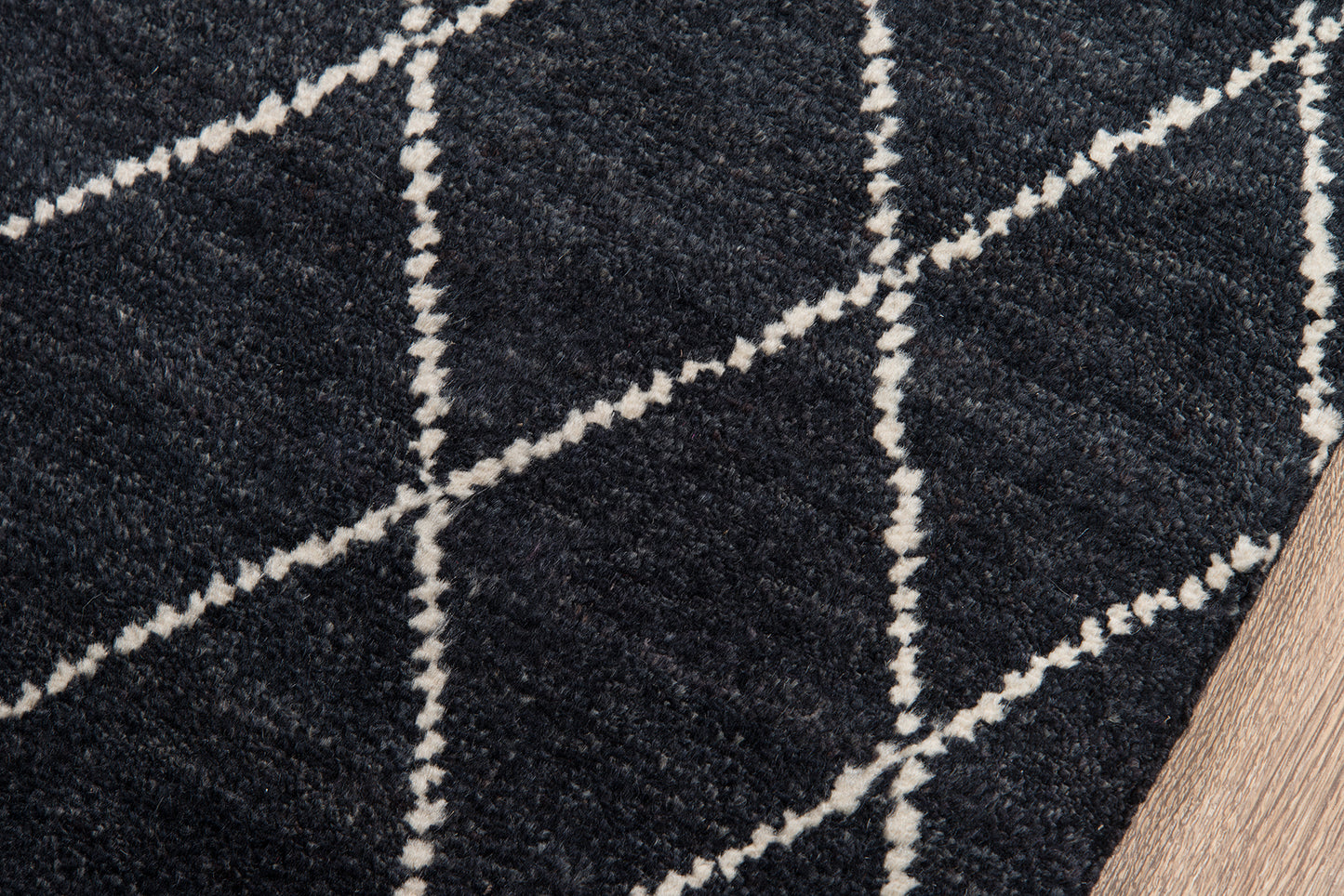 Navy blue rug with white geometric diamond lattice pattern; woven texture on wood floor.