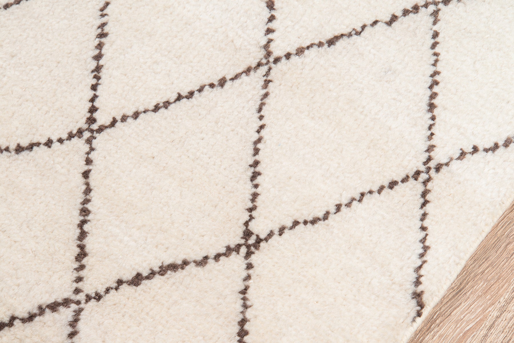 Beige rug with dark brown diagonal grid/diamond pattern, soft texture, on light wood floor.