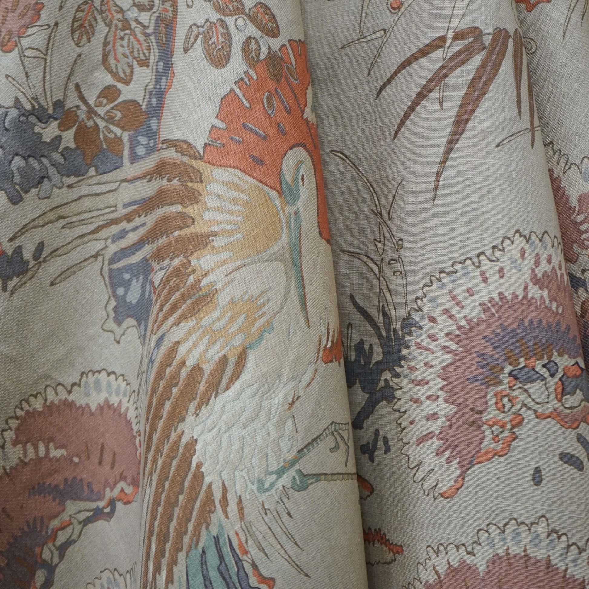 Beige linen fabric with a toile-style print featuring cranes, pink flowers, and muted blues and browns in a flowing drape.