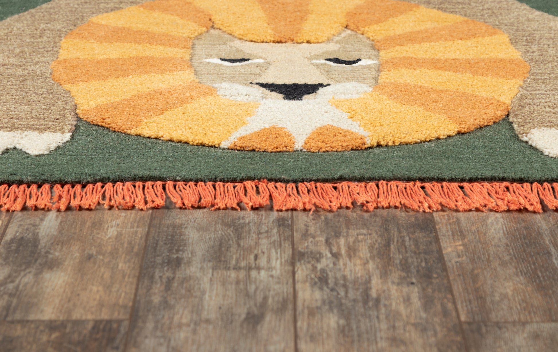 Lion face rug with orange mane, green background, orange fringe along bottom on wooden floor.