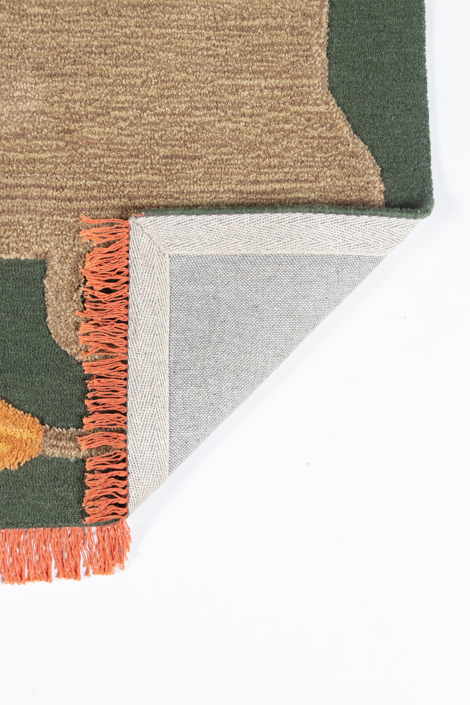 Woven geometric area rug in olive green and tan with orange fringe; folded corner shows gray backing.