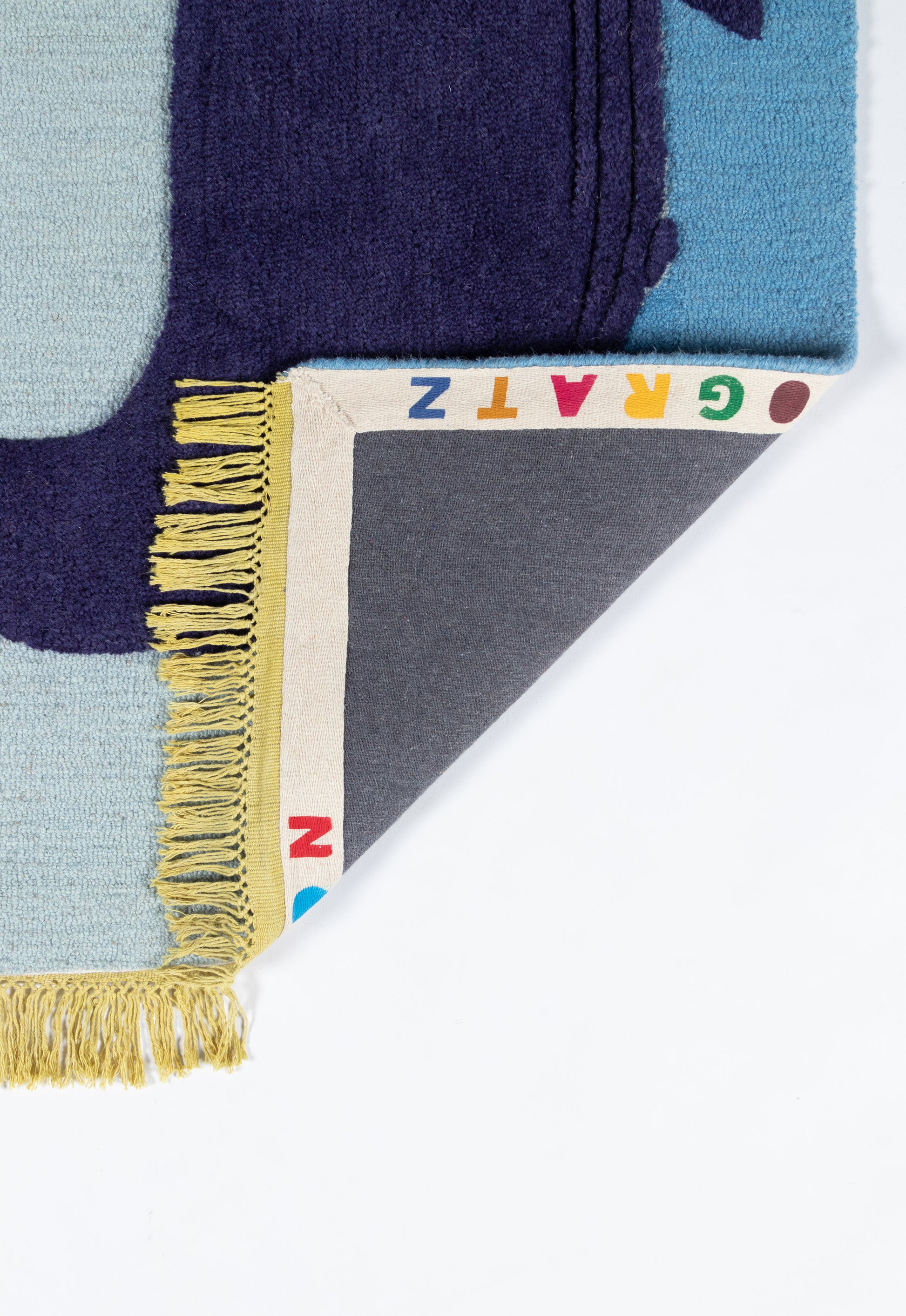 Blue geometric rug with cream fringe, white border featuring multicolor alphabet letters and a gray underside.