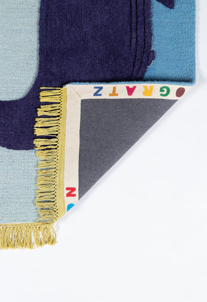 Wool area rug with geometric blue blocks, navy and light blue, yellow fringe; folded corner shows multicolor alphabet edge.