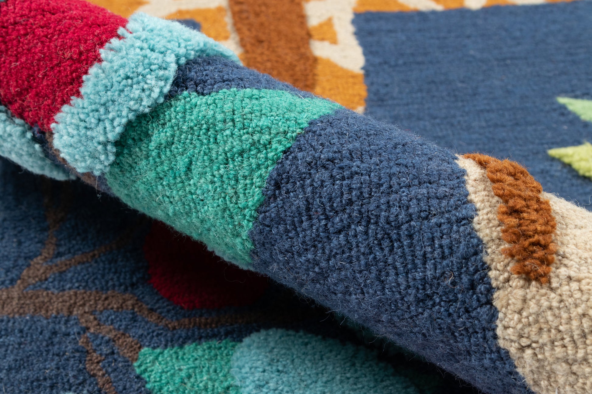Close-up of a multicolor tufted rug with thick pile in teal, blue, red, brown and beige geometric pattern.