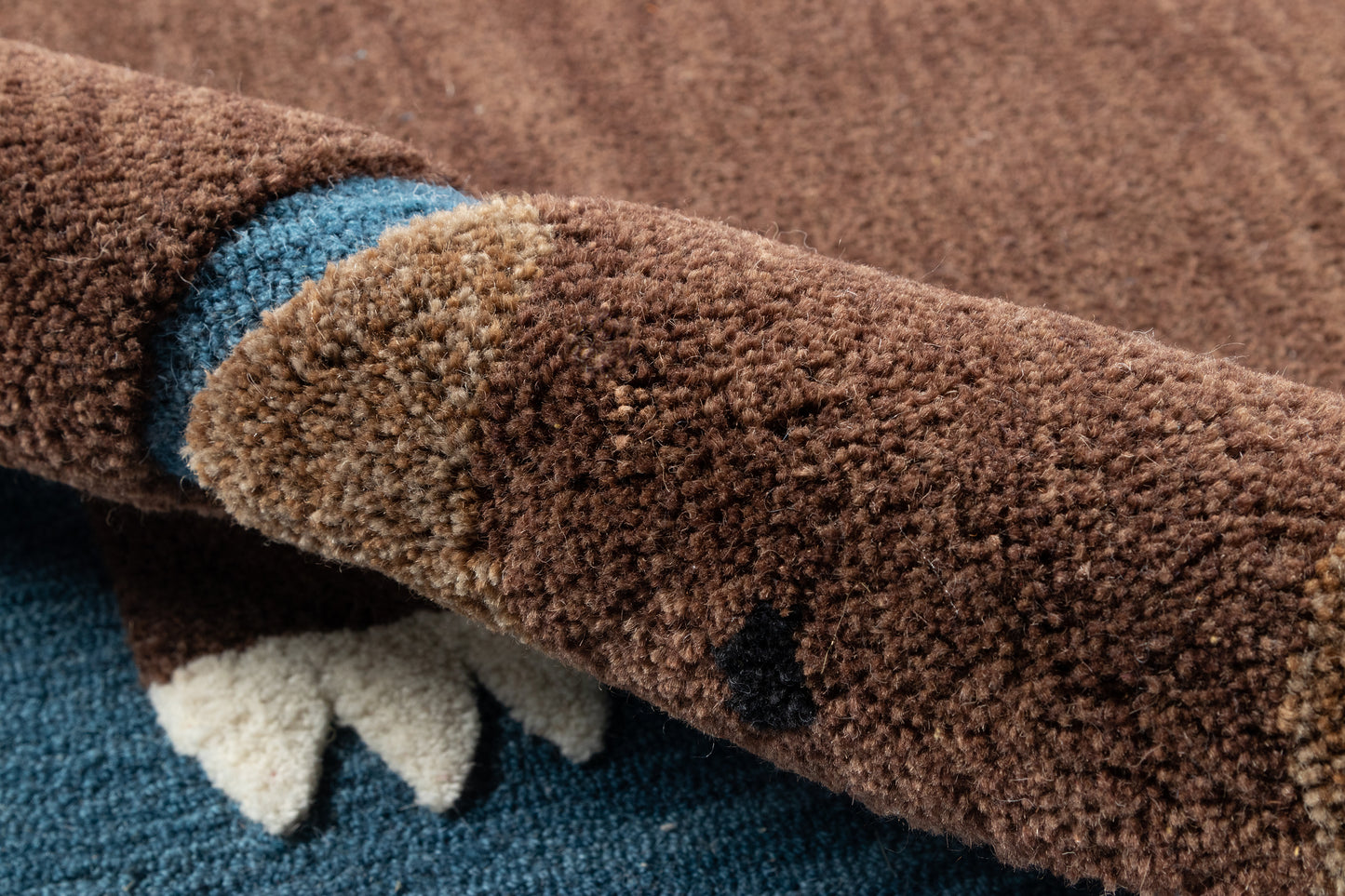 Close-up of a brown plush shag rug with blue and white accents; thick textured pile and folded edge.