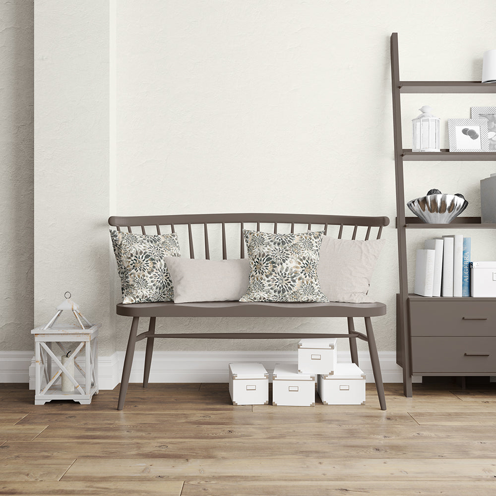Dark brown wooden bench with slatted back and tapered legs, two floral cushions and two beige cushions in a neutral living room.