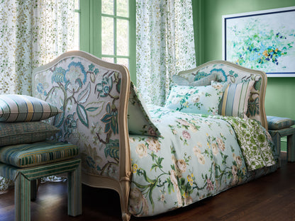 Two vintage floral upholstered beds with carved wooden frames and pale blue-green bedding against green walls.