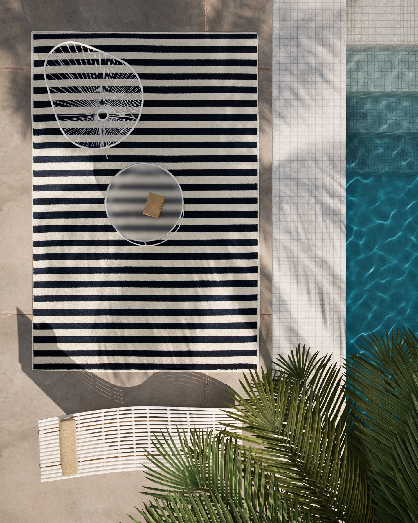 Outdoor rectangular black-and-white striped rug, round glass tray and circular metal decor on it, poolside with palm fronds.