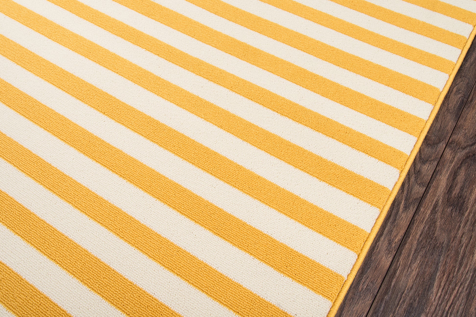 Rectangular yellow and white striped woven cotton rug on dark wood floor.