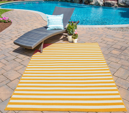 Yellow and white striped outdoor rug on brick patio beside a gray wicker lounge chair with blue-striped pillow near pool.