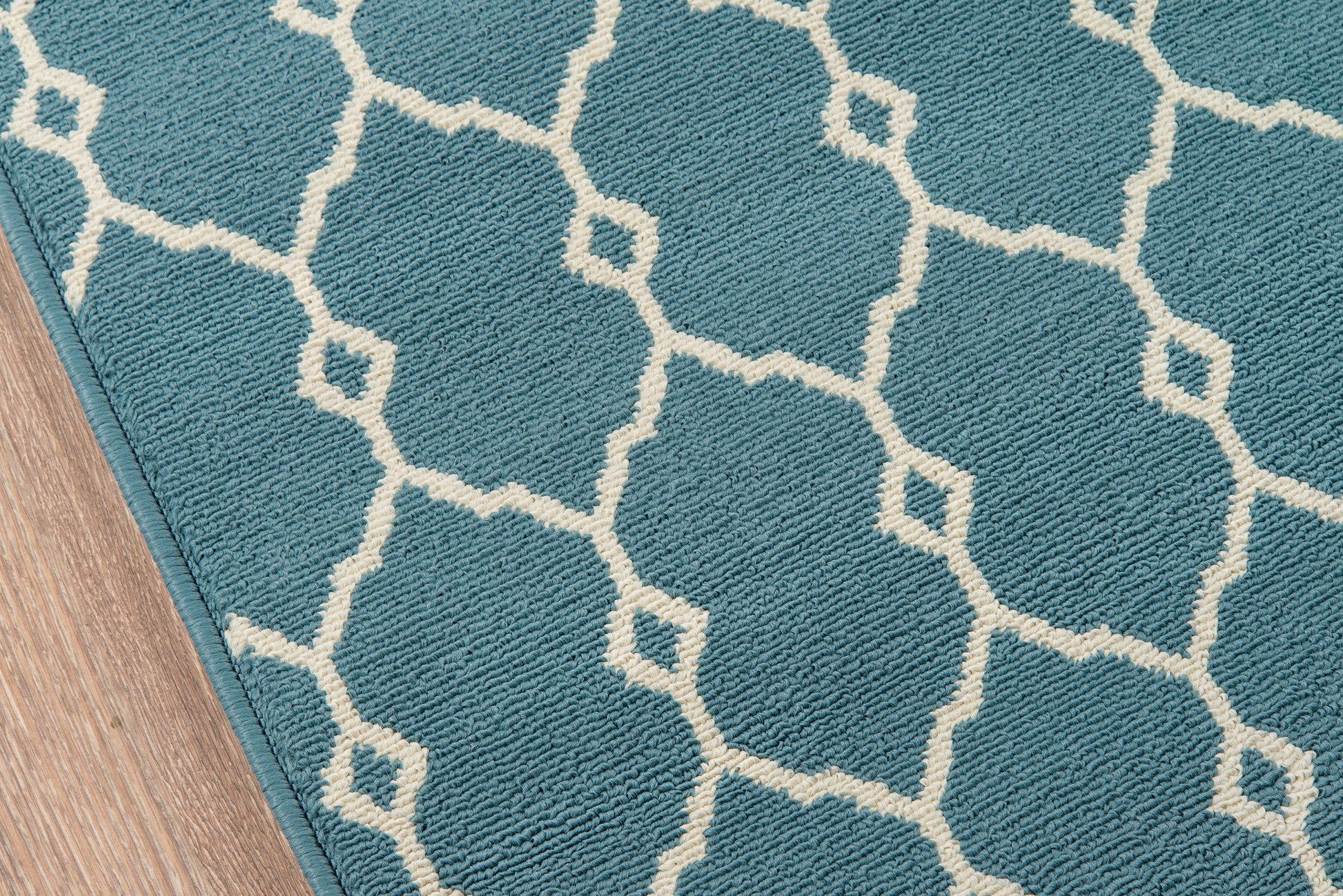 Blue geometric rug with white trellis lattice pattern on a wooden floor.