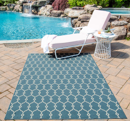 Poolside white lounge chair with cushion, round white side table, and blue geometric trellis rug on brick patio.