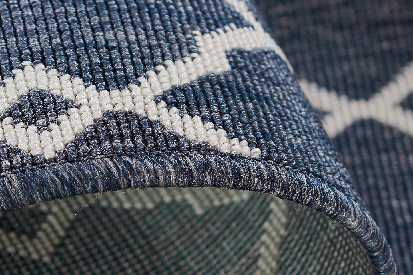 Close-up of blue woven rug with white geometric lattice pattern; textured weave and folded edge.