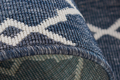 Close-up of blue woven rug with white geometric lattice pattern; textured weave and folded edge.